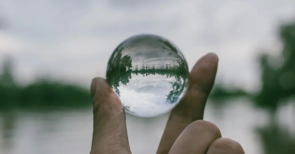 Can journaling make you think more clearly? A hand holding a clear glass sphere that refracts and sharpens a blurred landscape — symbolizing how writing can bring thoughts into focus and offer a new perspective.
